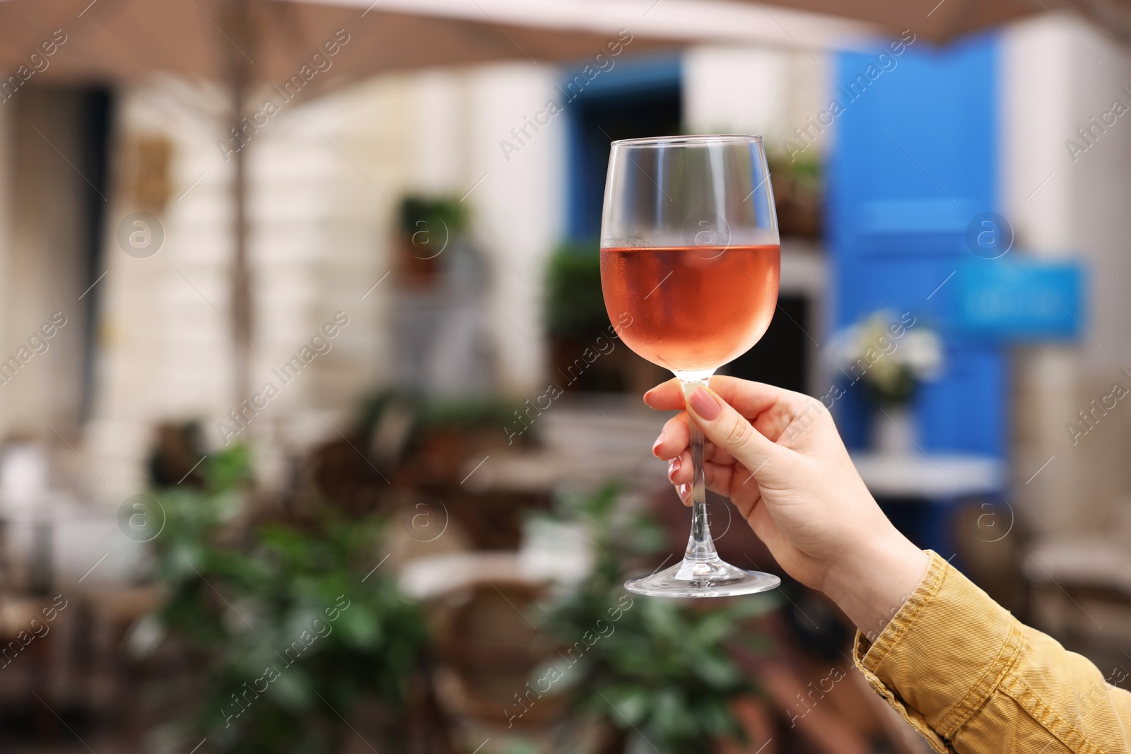 Photo of Woman holding glass of rose wine outdoors, closeup. Space for text