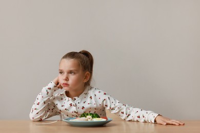 Photo of Cute little girl refusing to eat her dinner at table on grey background, space for text