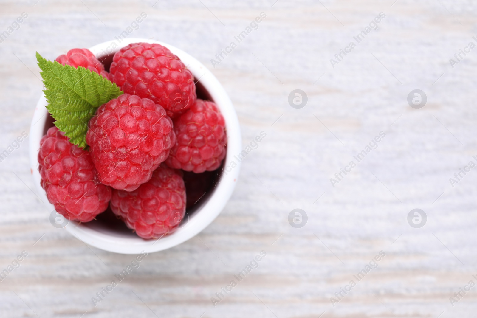Photo of Tasty ripe raspberries and green leaf on white wooden table, top view. Space for text
