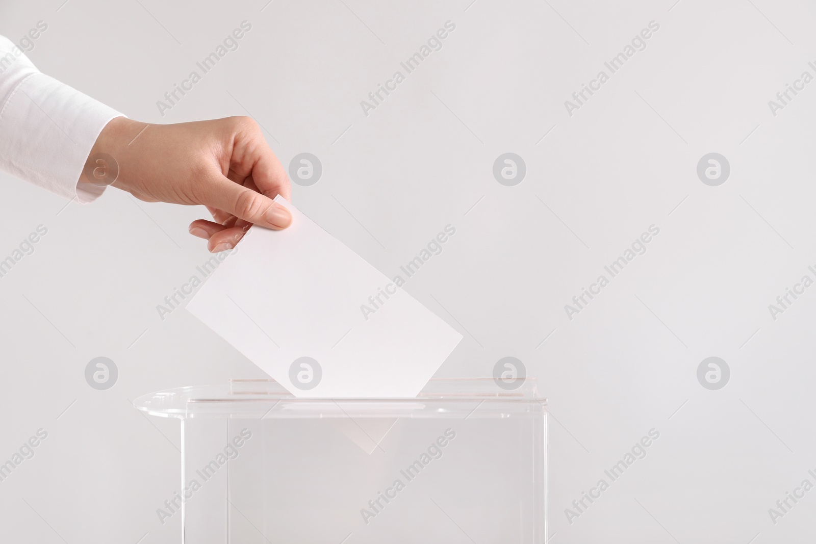 Photo of Woman putting her vote into ballot box on light grey background, closeup. Space for text