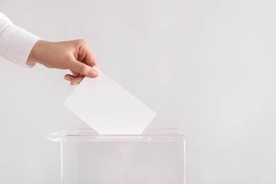 Woman putting her vote into ballot box on light grey background, closeup. Space for text