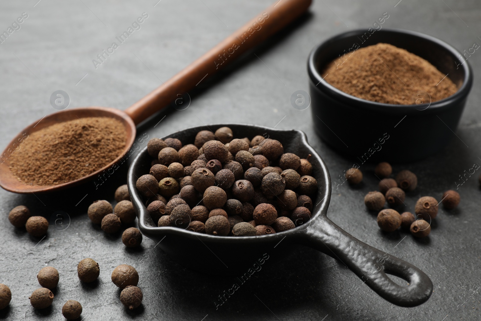 Photo of Ground and whole allspice berries (Jamaica pepper) on black table, closeup