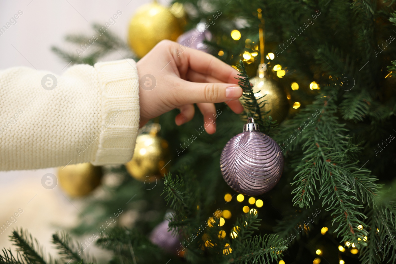 Photo of Woman decorating fir tree with golden Christmas ball indoors, closeup