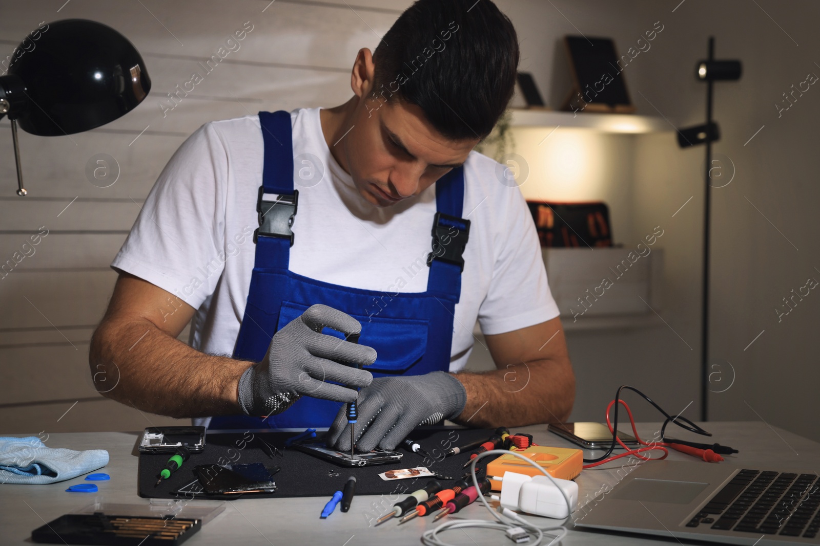 Photo of Technician repairing broken smartphone at table indoors