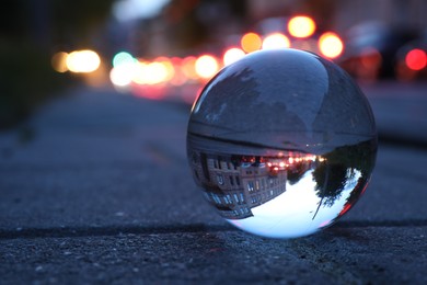 Photo of Beautiful city street, overturned reflection. Crystal ball on asphalt road outdoors, closeup. Space for text
