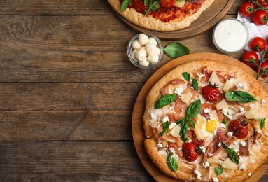 Photo of Delicious pita pizzas with prosciutto, pineapple, grilled tomatoes and egg on wooden table, flat lay. Space for text