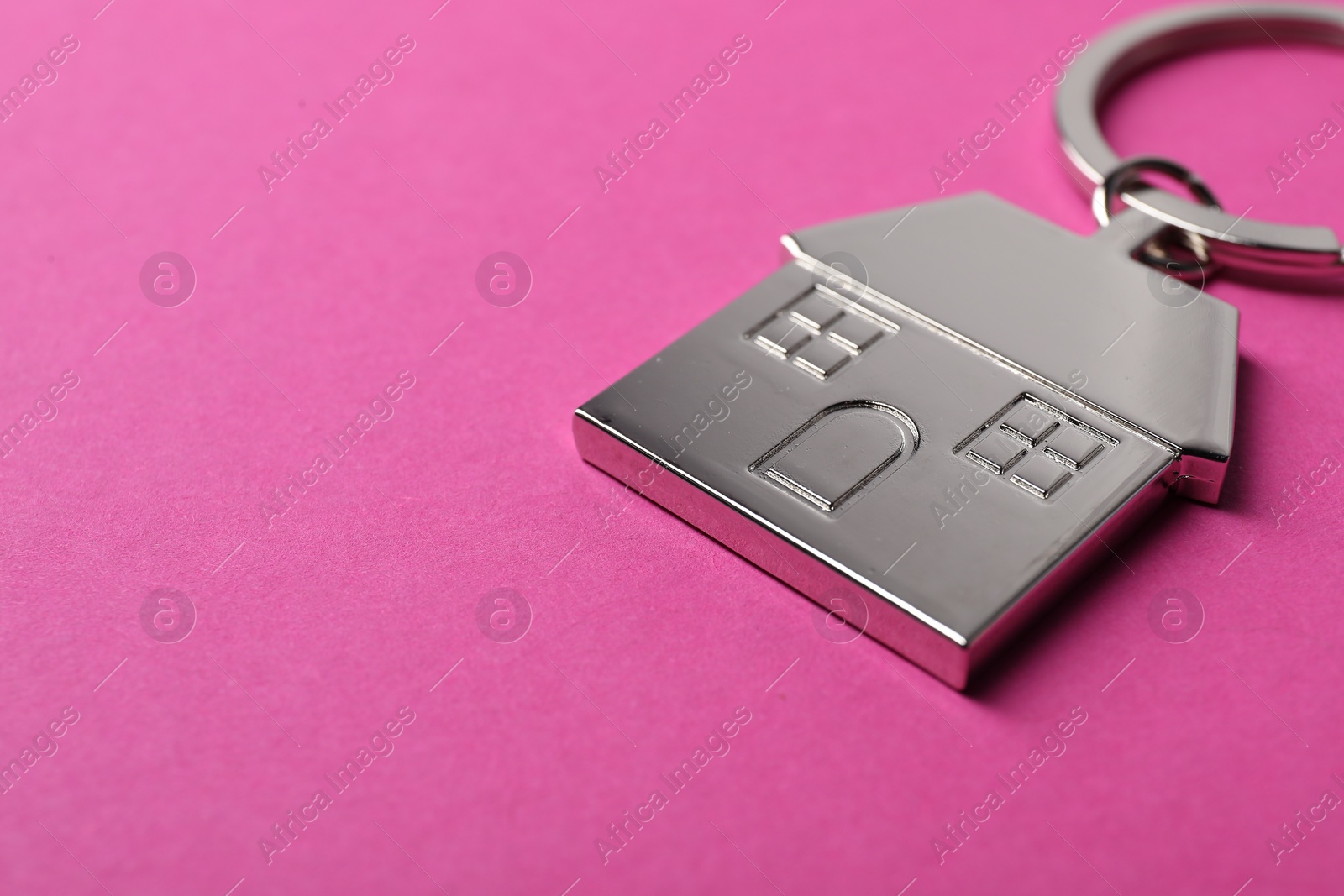 Photo of Metallic keychain in shape of house on bright pink background, closeup. Space for text