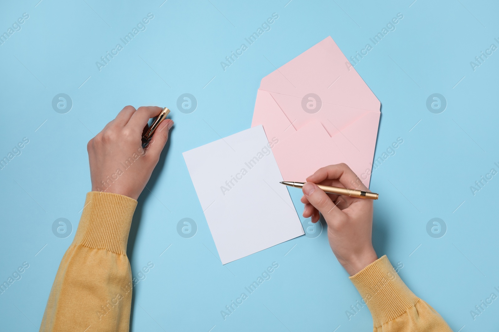 Photo of Woman writing letter at light blue table, top view. Space for text