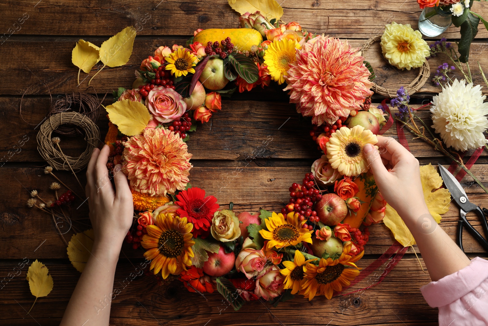 Photo of Florist making beautiful autumnal wreath with flowers and fruits at wooden table, top view