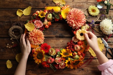 Photo of Florist making beautiful autumnal wreath with flowers and fruits at wooden table, top view