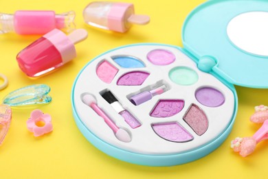 Photo of Decorative cosmetics for kids. Eye shadow palette, lipsticks and accessories on yellow background, closeup