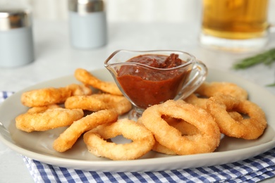 Photo of Delicious crunchy fried onion rings and sauce on grey table, closeup