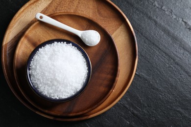 Photo of Organic white salt in bowl and spoon on black table, top view. Space for text