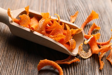 Photo of Scoop with dry orange peels on wooden table, closeup