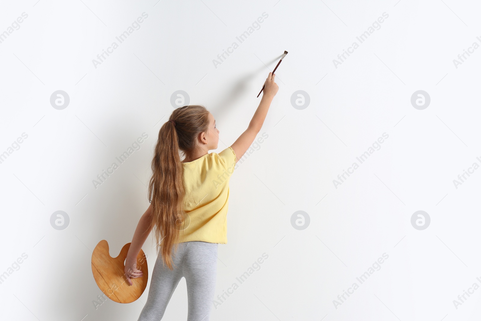 Photo of Little child painting on blank white wall indoors, space for text