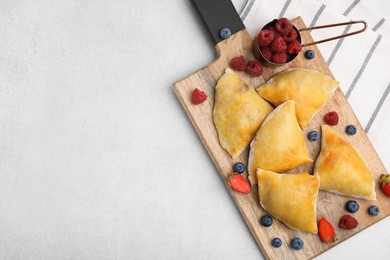 Wooden board with delicious samosas and berries on light table, top view. Space for text