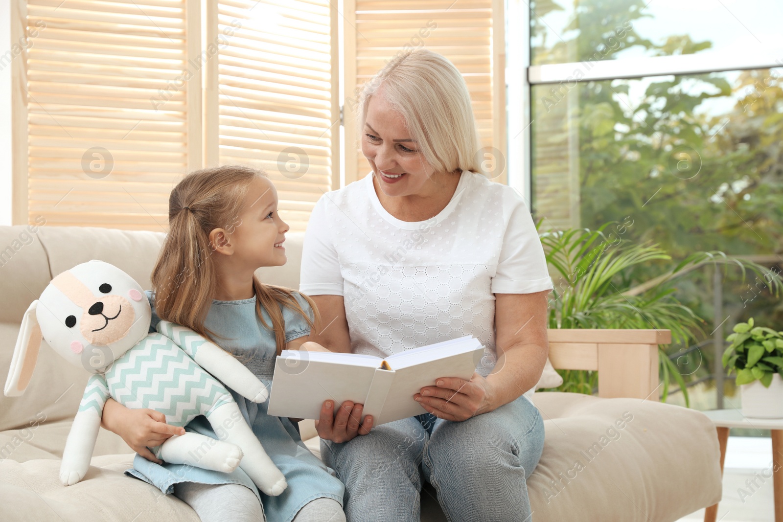 Photo of Happy grandmother with her granddaughter reading book together at home