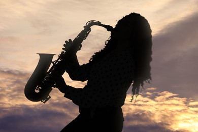Image of Silhouette of woman playing saxophone against beautiful sky at sunset