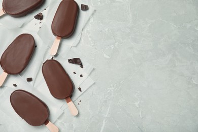 Photo of Glazed ice cream bars and chocolate chunks on light grey table, flat lay. Space for text