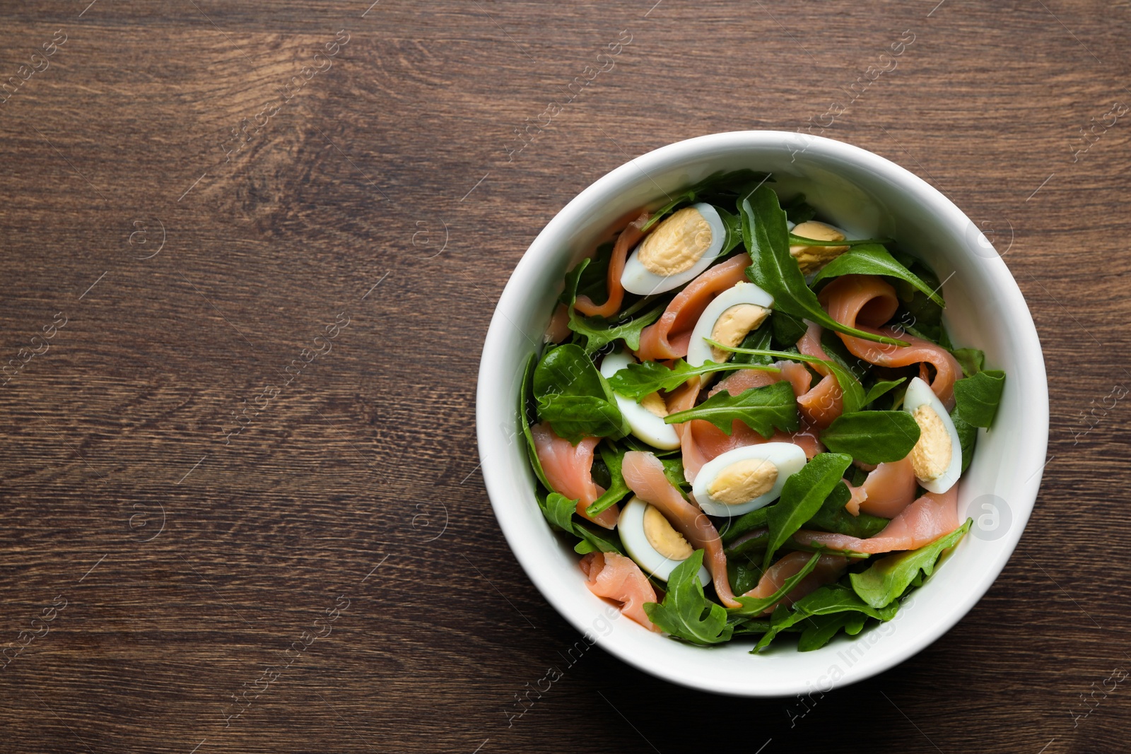 Photo of Delicious salad with boiled eggs, salmon and arugula on wooden table, top view. Space for text