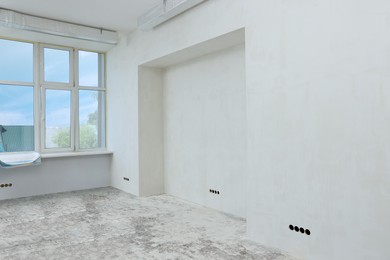 Photo of Empty room with white wall and windows prepared for renovation