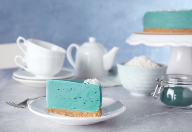 Piece of tasty spirulina cheesecake on grey table against blue background