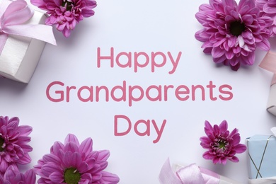 Gift boxes, beautiful pink flowers and phrase Happy Grandparents Day on white background, flat lay