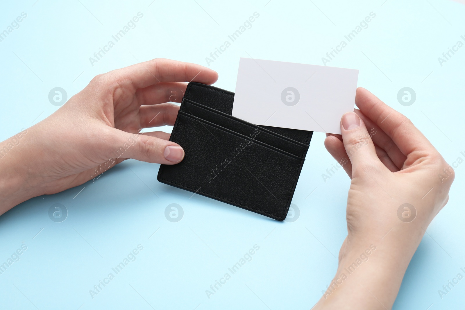 Photo of Woman holding business card holder with blank card on light blue background, closeup