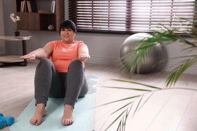 Photo of Overweight mature woman doing abs exercise on yoga mat at home, space for text