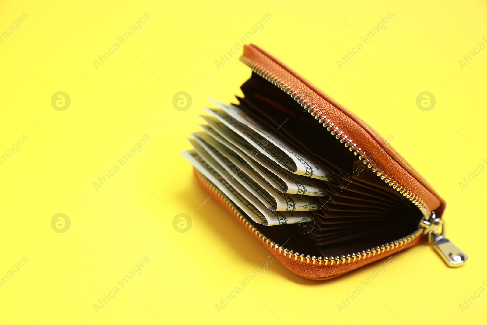 Photo of Stylish brown leather purse with dollar banknotes on yellow background. Space for text