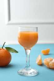 Photo of Delicious tangerine liqueur and fresh fruits on light blue wooden table