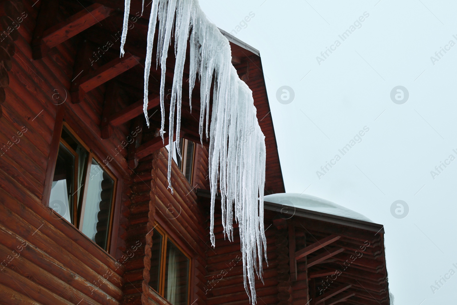 Photo of House with icicles on roof, low angle view. Winter season