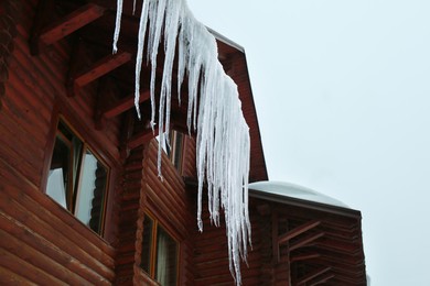 House with icicles on roof, low angle view. Winter season