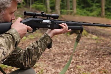 Photo of Man wearing camouflage and aiming with hunting rifle in forest, closeup