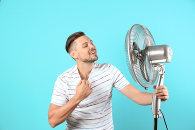 Photo of Man refreshing from heat in front of fan on color background
