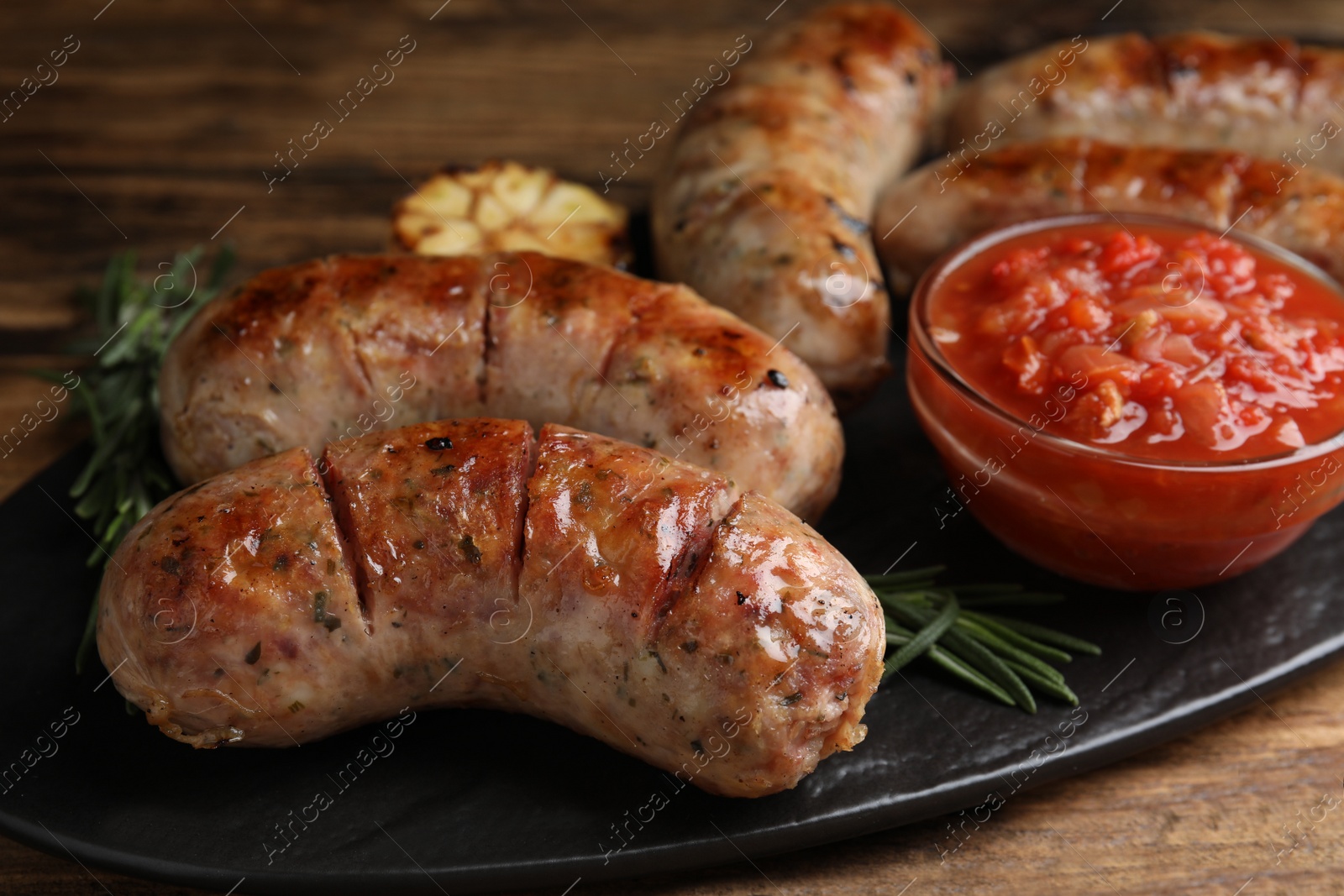 Photo of Tasty grilled sausages served with sauce on wooden table