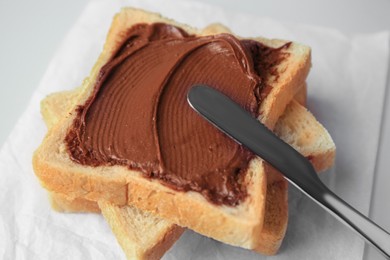 Photo of Tasty toast with chocolate paste and knife on light background, closeup