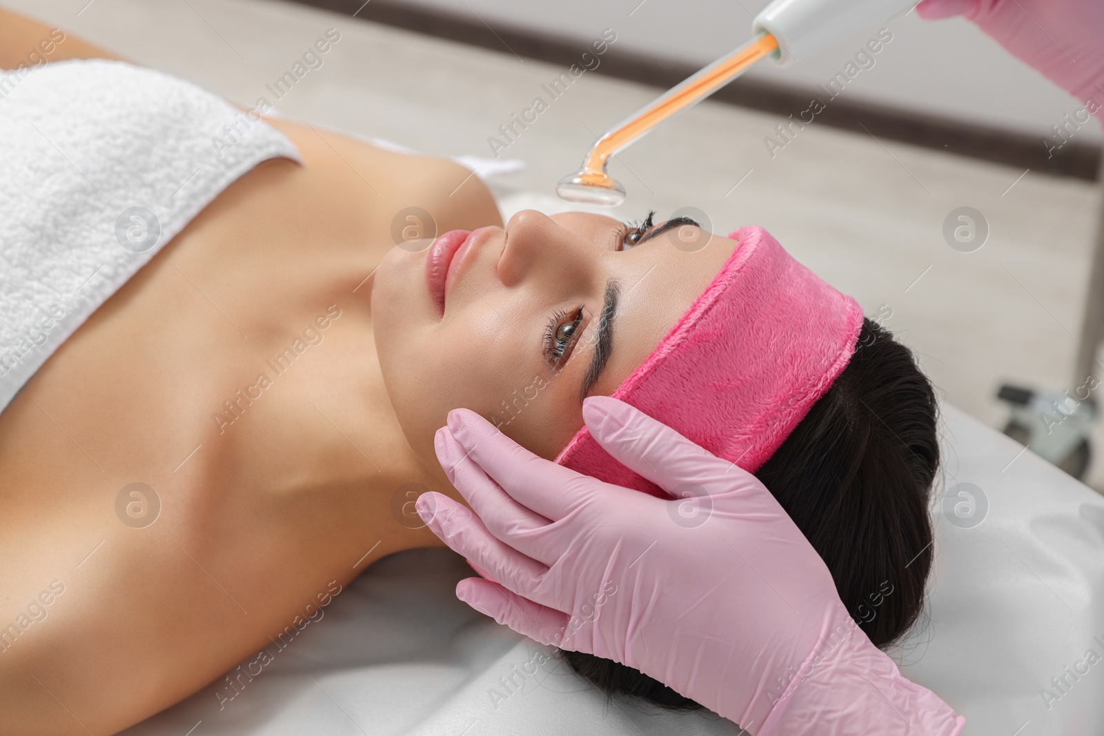 Photo of Young woman undergoing face rejuvenation procedure with darsonval in salon