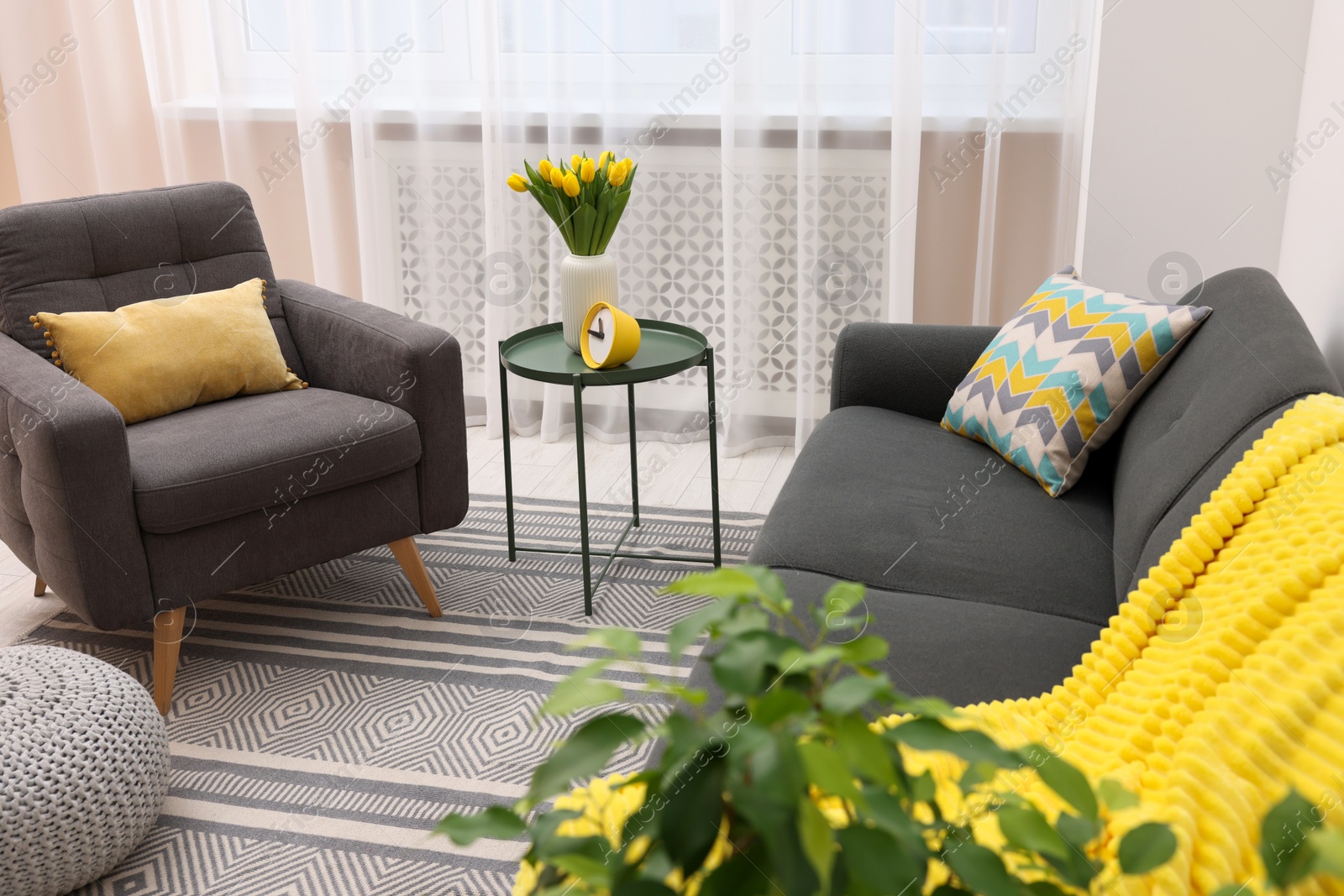 Photo of Spring atmosphere. Stylish living room interior with comfortable furniture and bouquet of beautiful yellow tulips