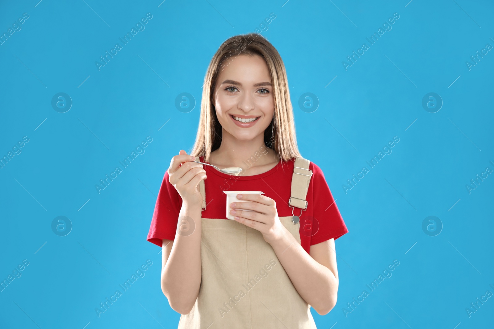 Photo of Young attractive woman with tasty yogurt on blue background