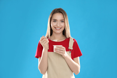 Photo of Young attractive woman with tasty yogurt on blue background