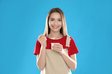 Young attractive woman with tasty yogurt on blue background