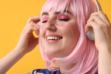 Photo of Happy woman with bright makeup and glitter freckles listening to music on yellow background, closeup