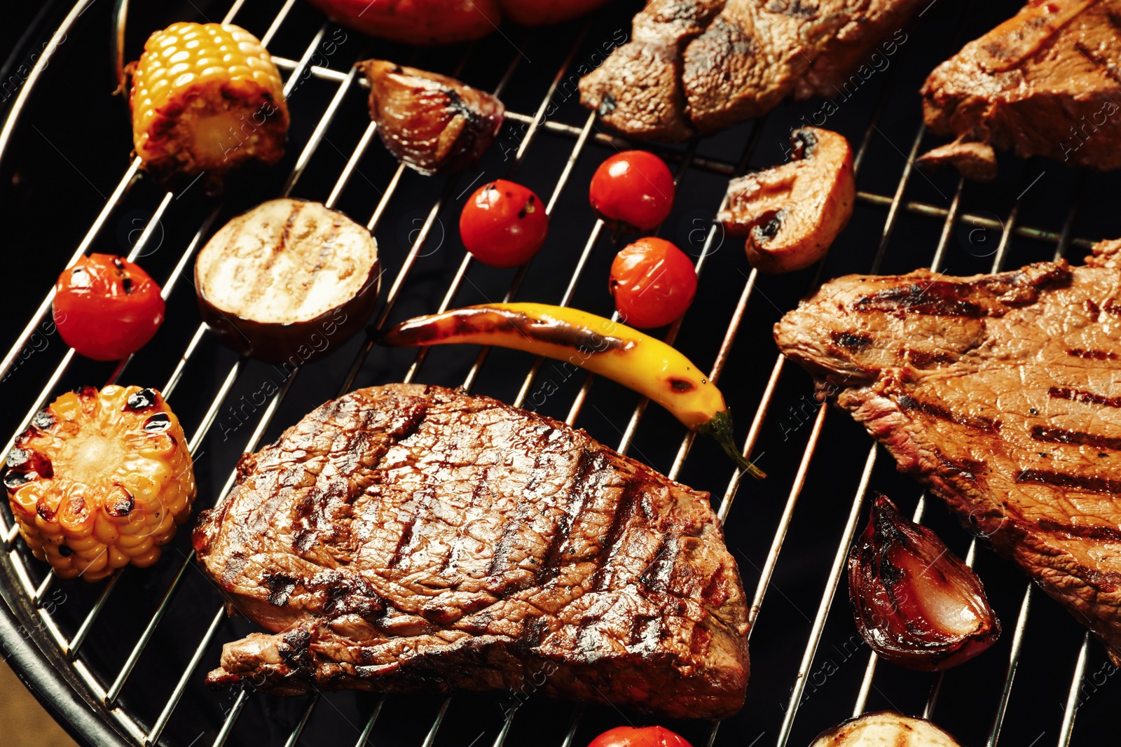 Photo of Fresh grilled meat steaks and vegetables on barbecue grate