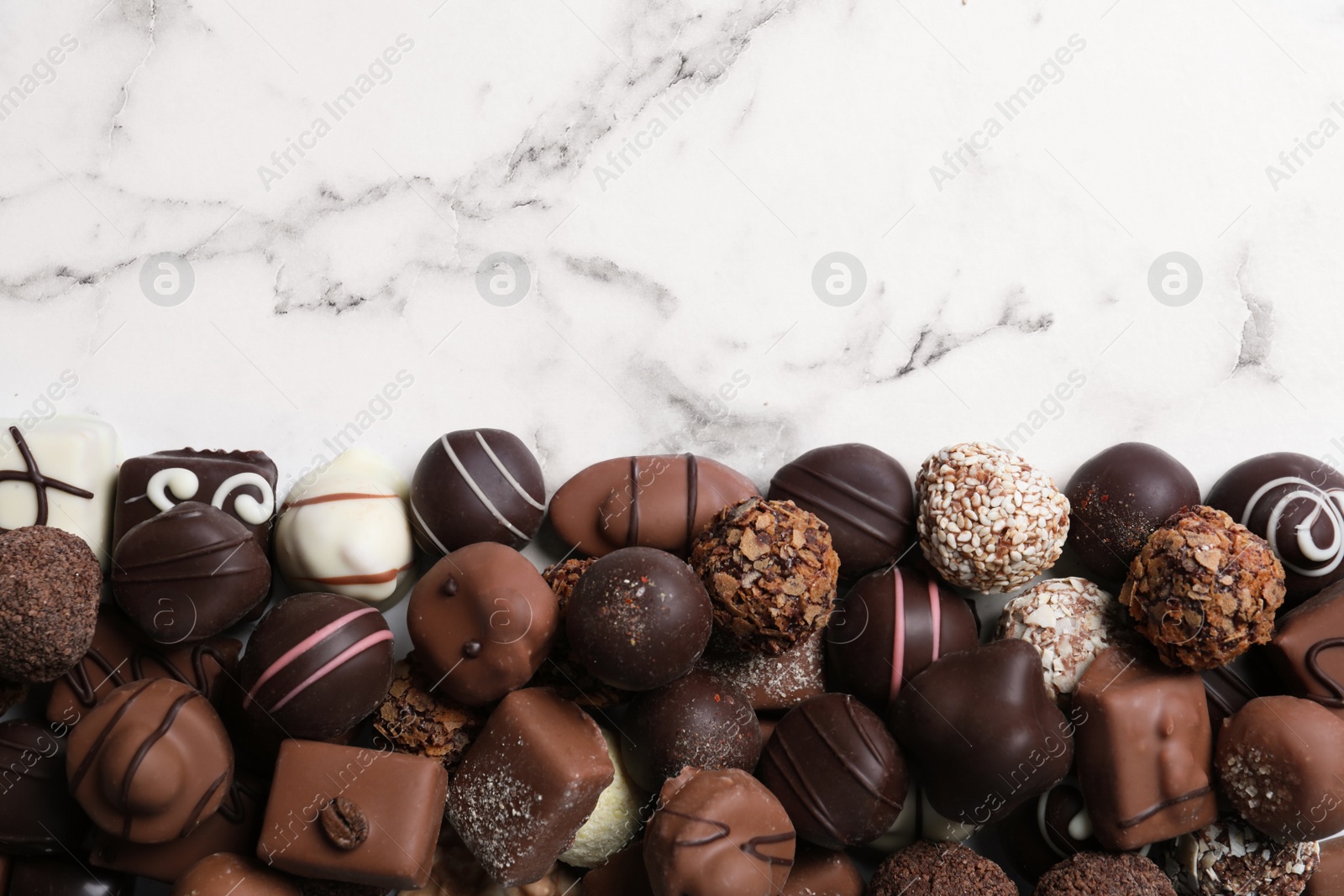 Photo of Different tasty chocolate candies on white marble table, flat lay. Space for text