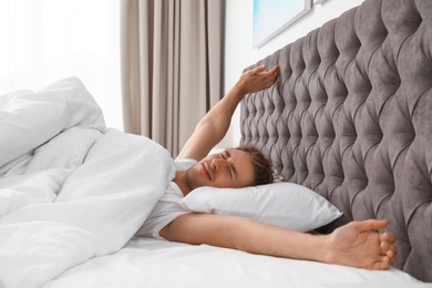 Sleepy young man stretching while lying under blanket in morning. Bedtime