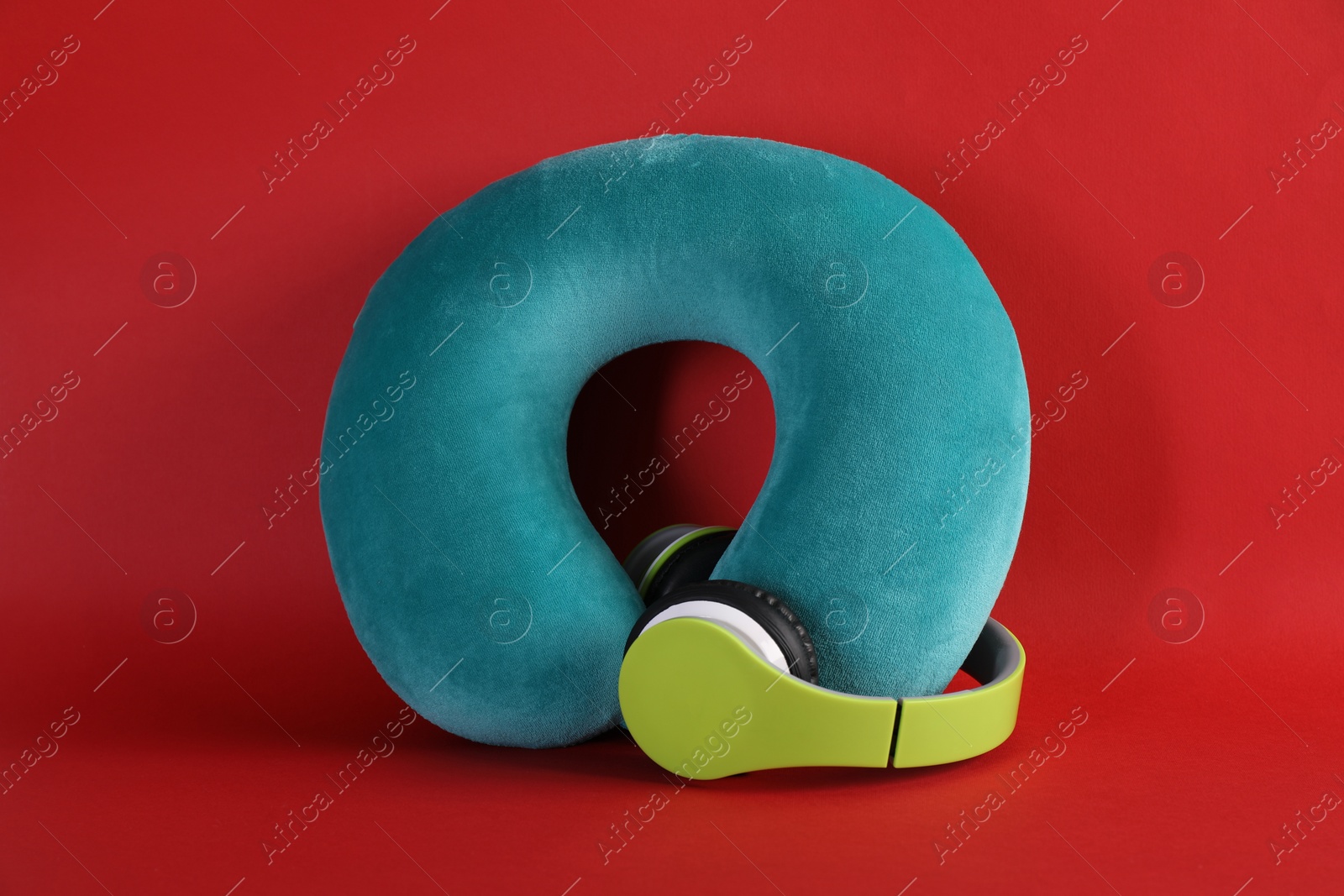 Photo of Turquoise travel pillow and headphones on red background