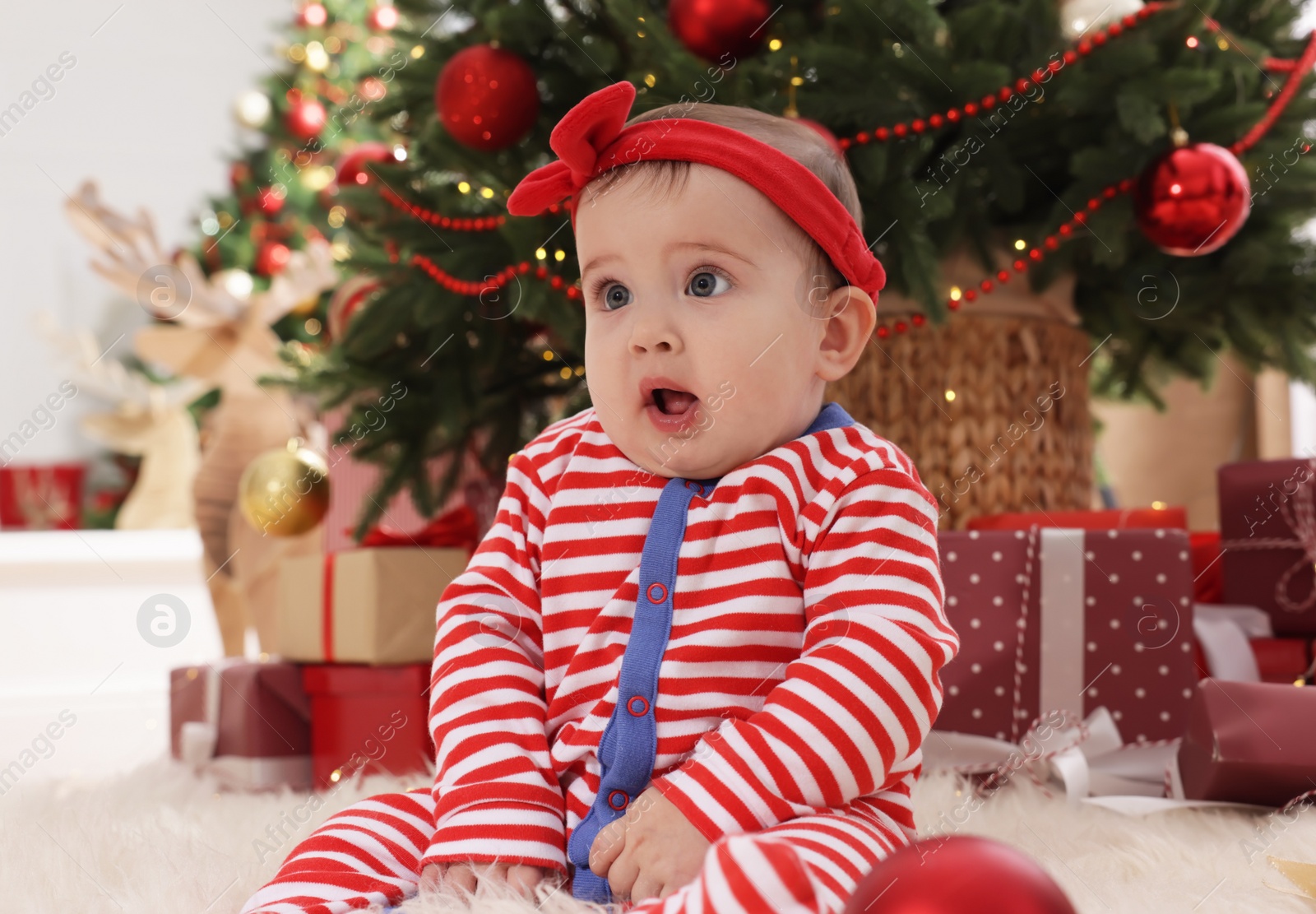 Photo of Baby wearing bright Christmas pajamas on floor in room