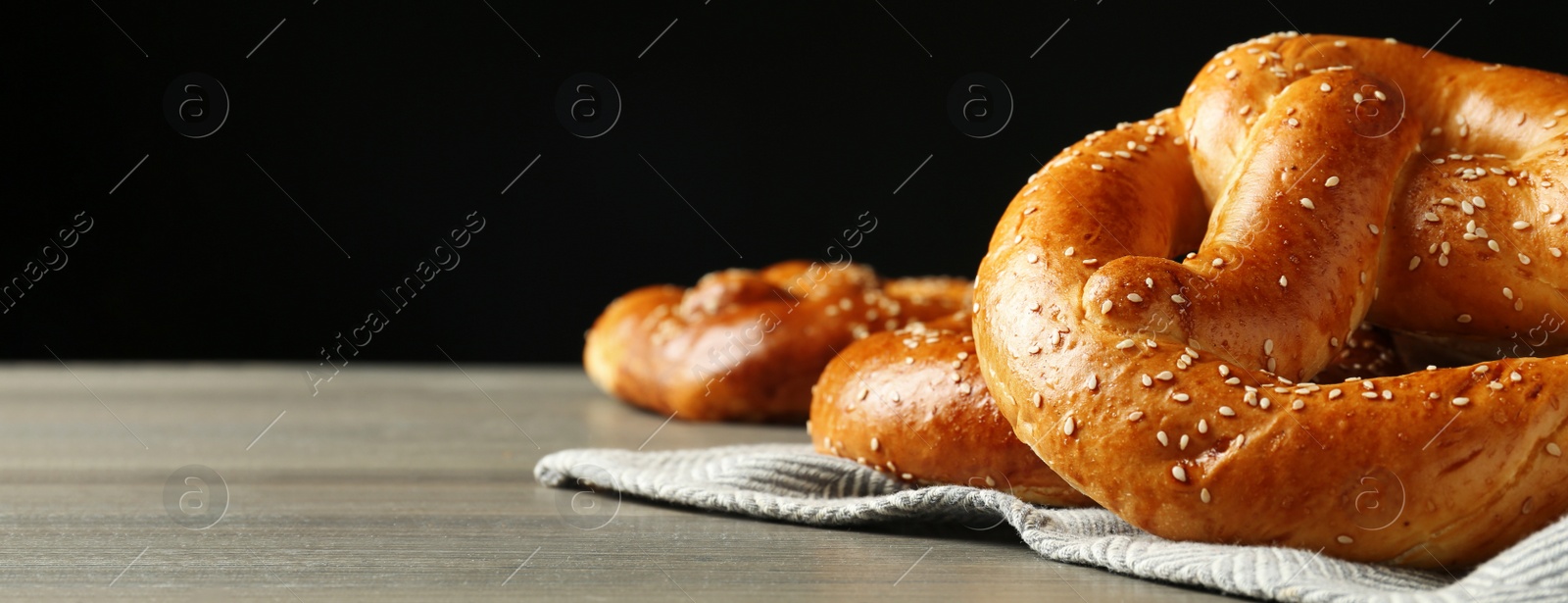 Image of Tasty freshly baked pretzels on wooden table against black background, space for text. Banner design