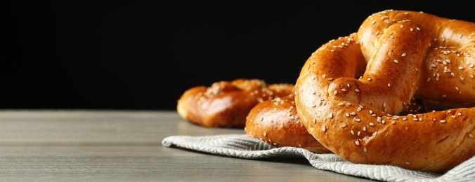 Image of Tasty freshly baked pretzels on wooden table against black background, space for text. Banner design